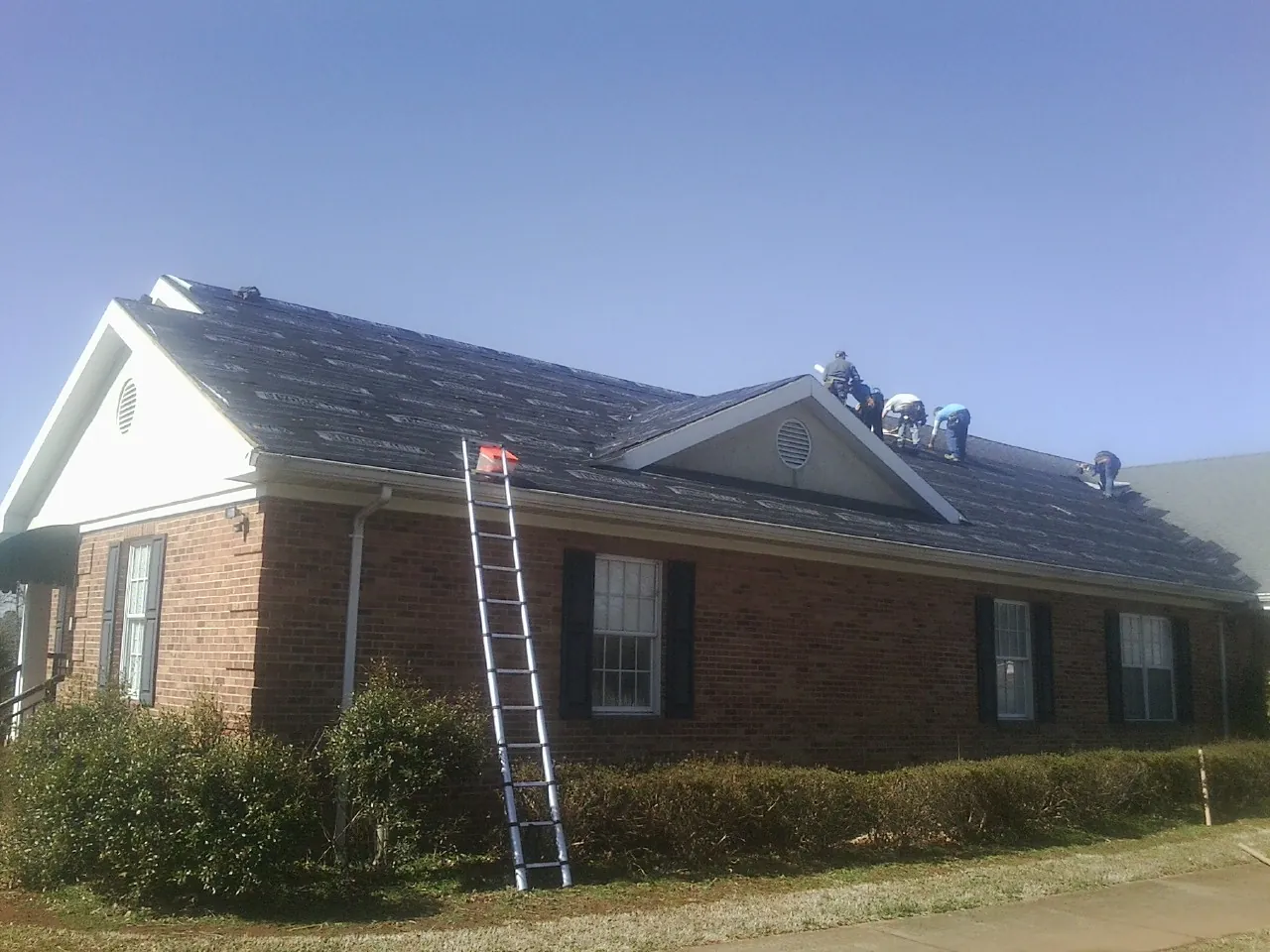 Crew tearing shingles off a brick ranch roof with a ladder set — Emergency Roof Repair work by our crew in Mooreville