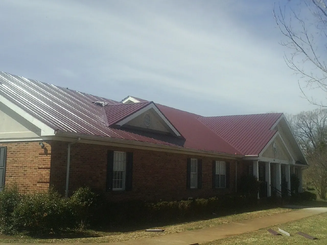 Red metal roof with gabled entries on a long brick building, from a Hail Damage Roof Repair job in Mooreville