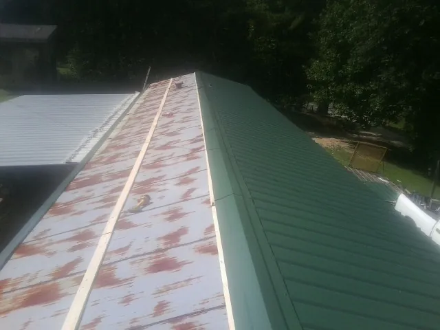 Old rusted panels beside newly installed green metal roofing — Wind Damage Roof Repair by Roofing Brothers in Mooreville