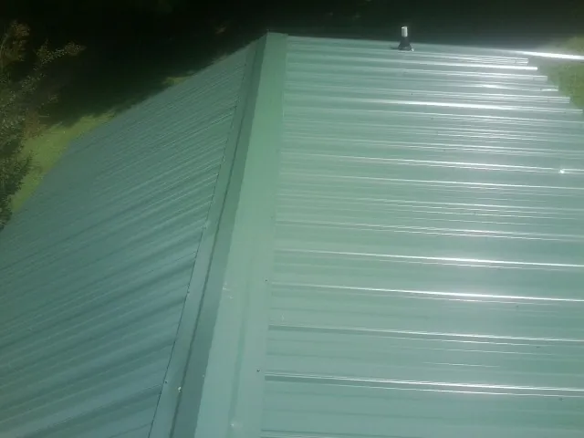 New green metal panels meeting at the ridge of a roof — Flat Roof Repair work by our crew in Mooreville