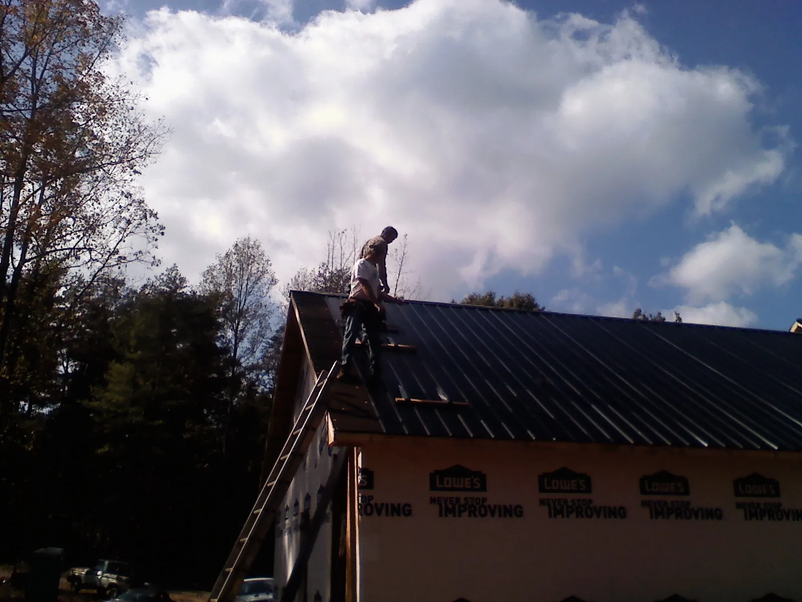 Roofer fastening dark metal panels high against a cloudy sky, from a Roof Inspection job in Mooreville
