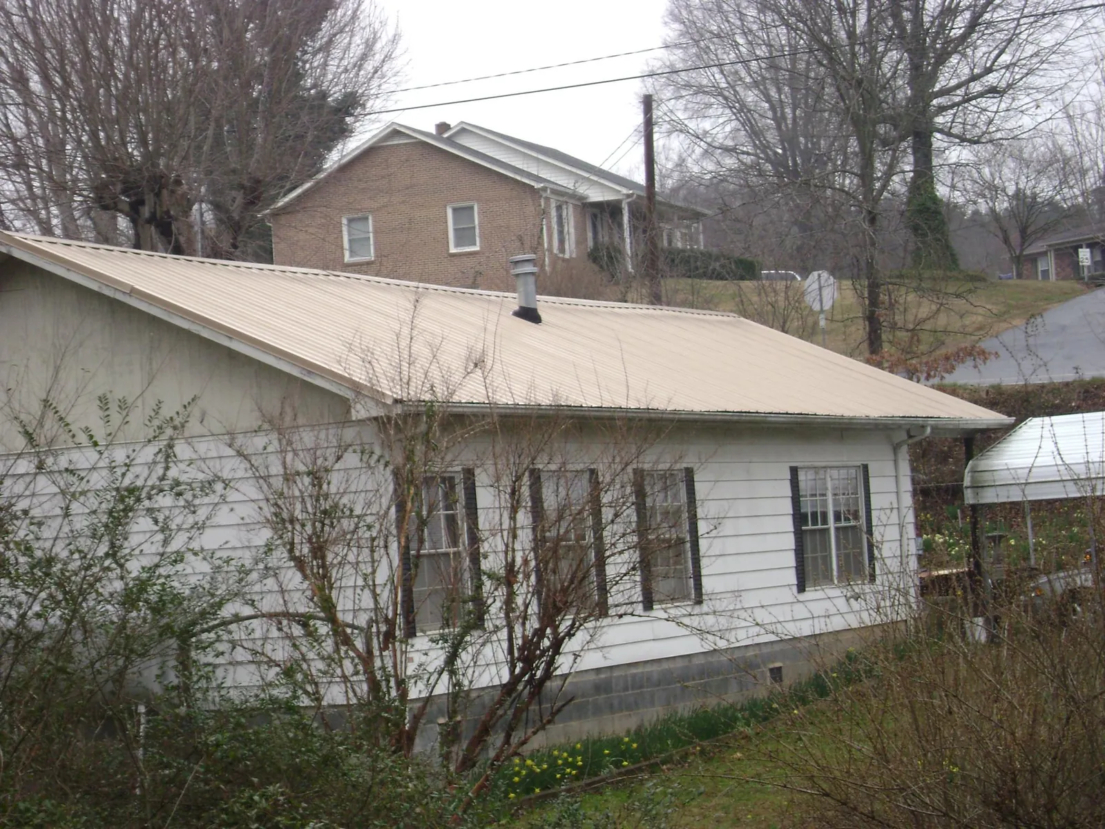 Tan metal roof on a white sided house set into a hillside — Commercial Roofing by Roofing Brothers in Mooreville