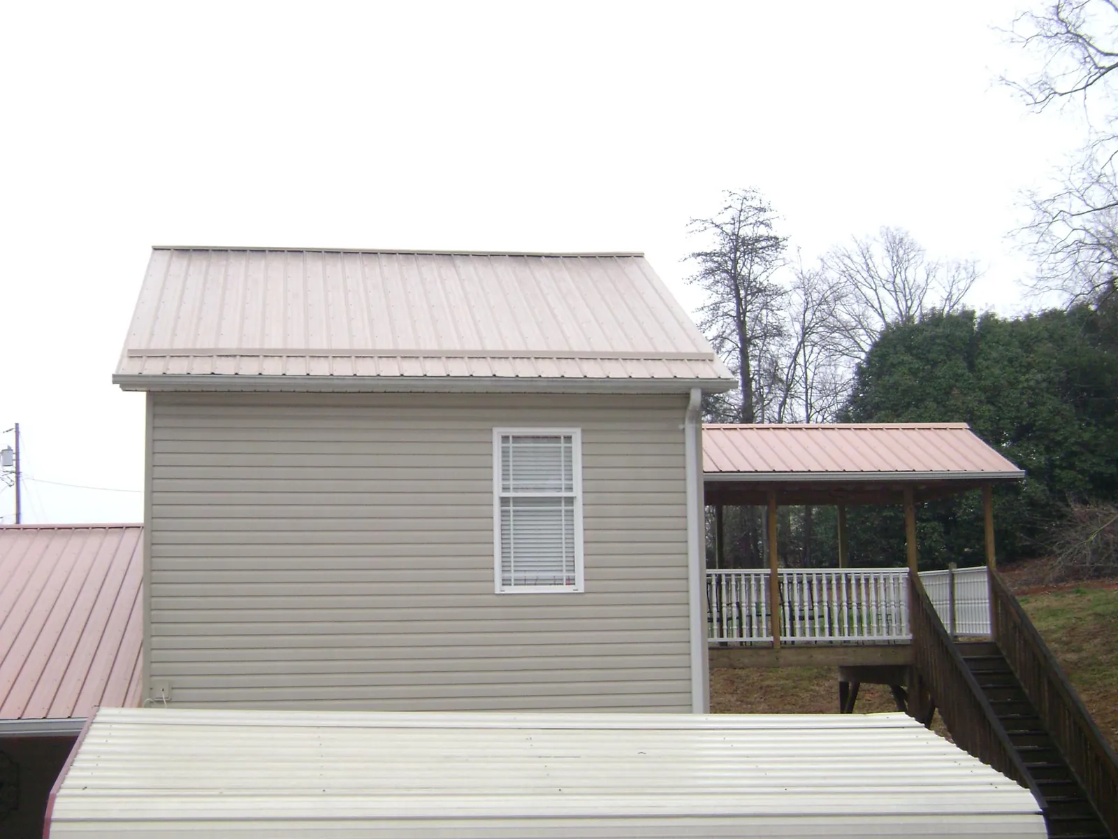 Tan metal roofs on a two story addition and attached porch, from a Roof Replacement job in Mooreville